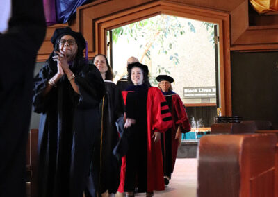 At the graduation ceremony, a group of people in academic regalia, including caps and gowns, walk in a line through a doorway. Colorful fabric drapes hang from the ceiling, and a "Black Lives Matter" sign is visible in the background, capturing this memorable event.